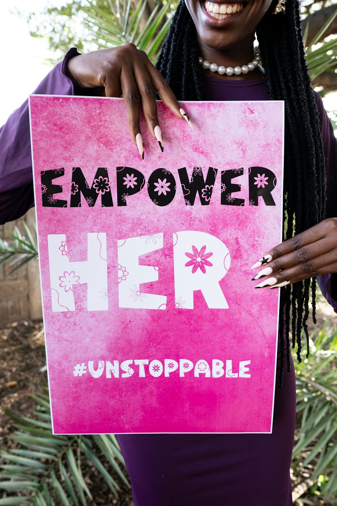 Woman holding a sign that says "empower her #unstoppable"